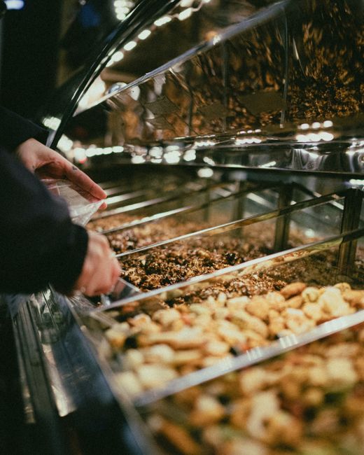 Hands selecting nuts and dried fruits from market display. Indoor lighting, close-up view. - Local vs. Imported Dry Fruits: A Comparison
