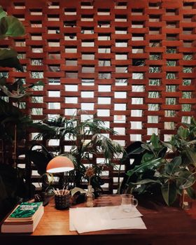 Warm indoor workspace with plants, books, and a stylish lamp against a brick wall, ideal for creative inspiration.