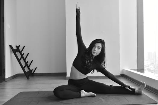 Young woman in black performing seated yoga stretch indoors, offering a calm fitness moment.