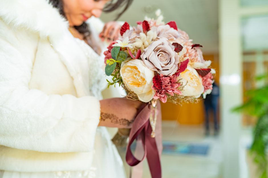 Close-up of a bride holding a beautiful floral bouquet with roses and ribbons, highlighting wedding elegance.