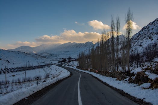 Captivating winter landscape featuring a winding road through snowy mountains under a dramatic sunset sky.