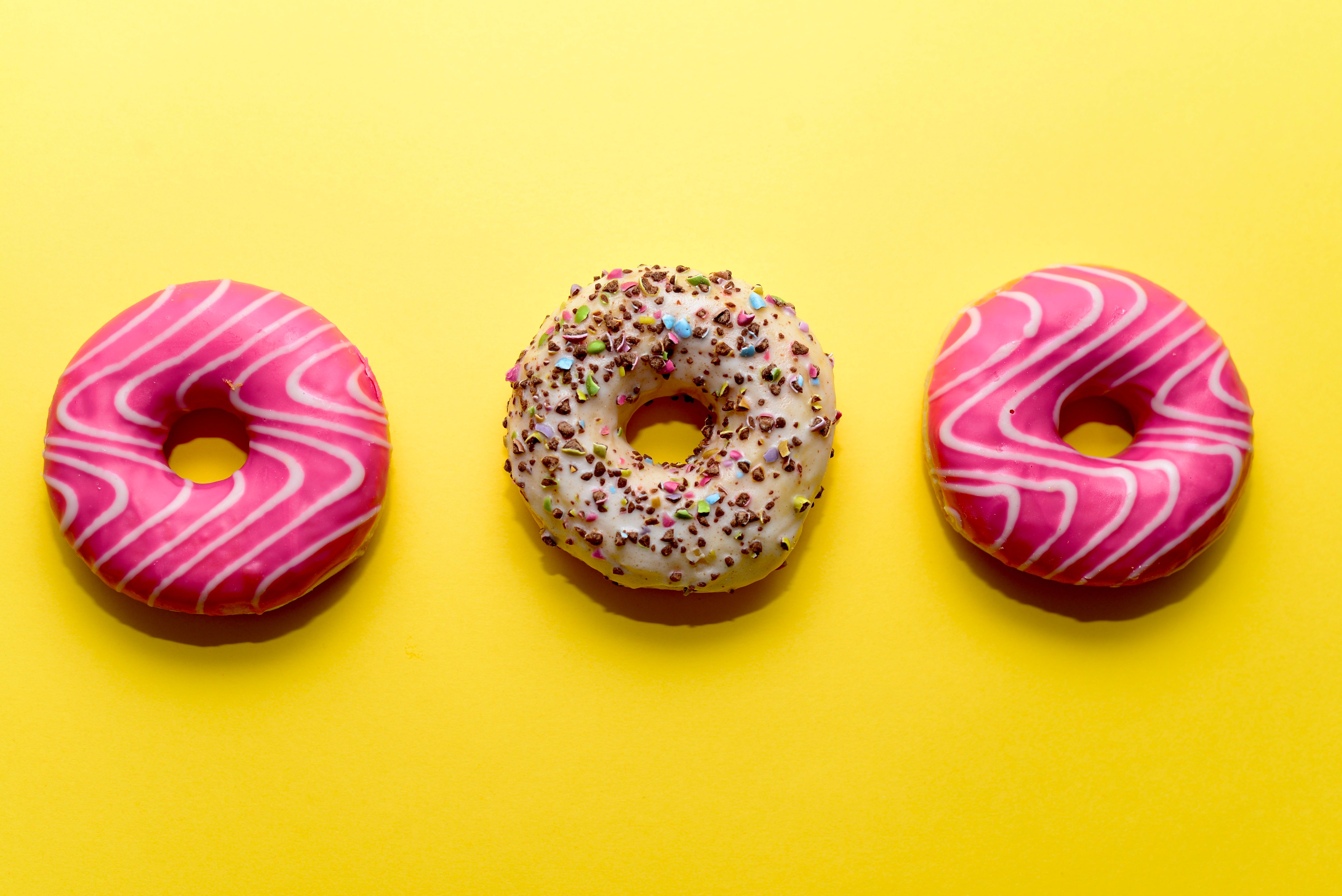 Three decorated donuts on a bright yellow background, a visual treat for dessert lovers.