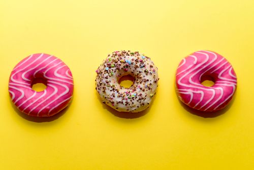 Free Three decorated donuts on a bright yellow background, a visual treat for dessert lovers. Stock Photo