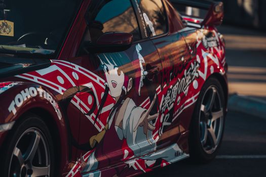 Close-up of a red sports car with bold anime-themed custom livery, showcasing urban street style.