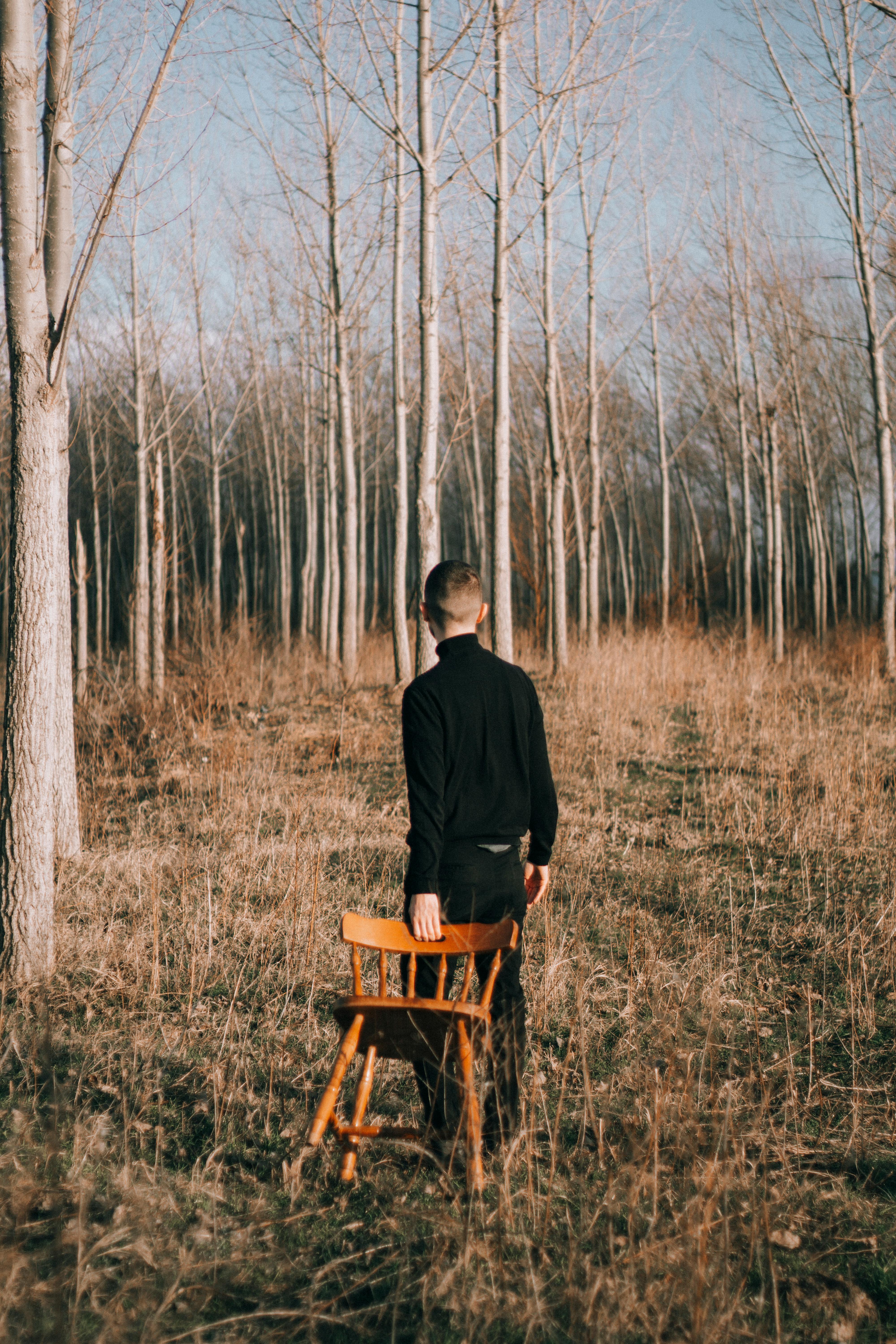 A man in black walks through a forest carrying a chair, capturing a serene winter scene in Novi Sad, Serbia.