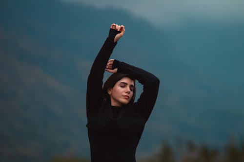 Free Woman Standing with Eyes Closed and Arms Raised Stock Photo