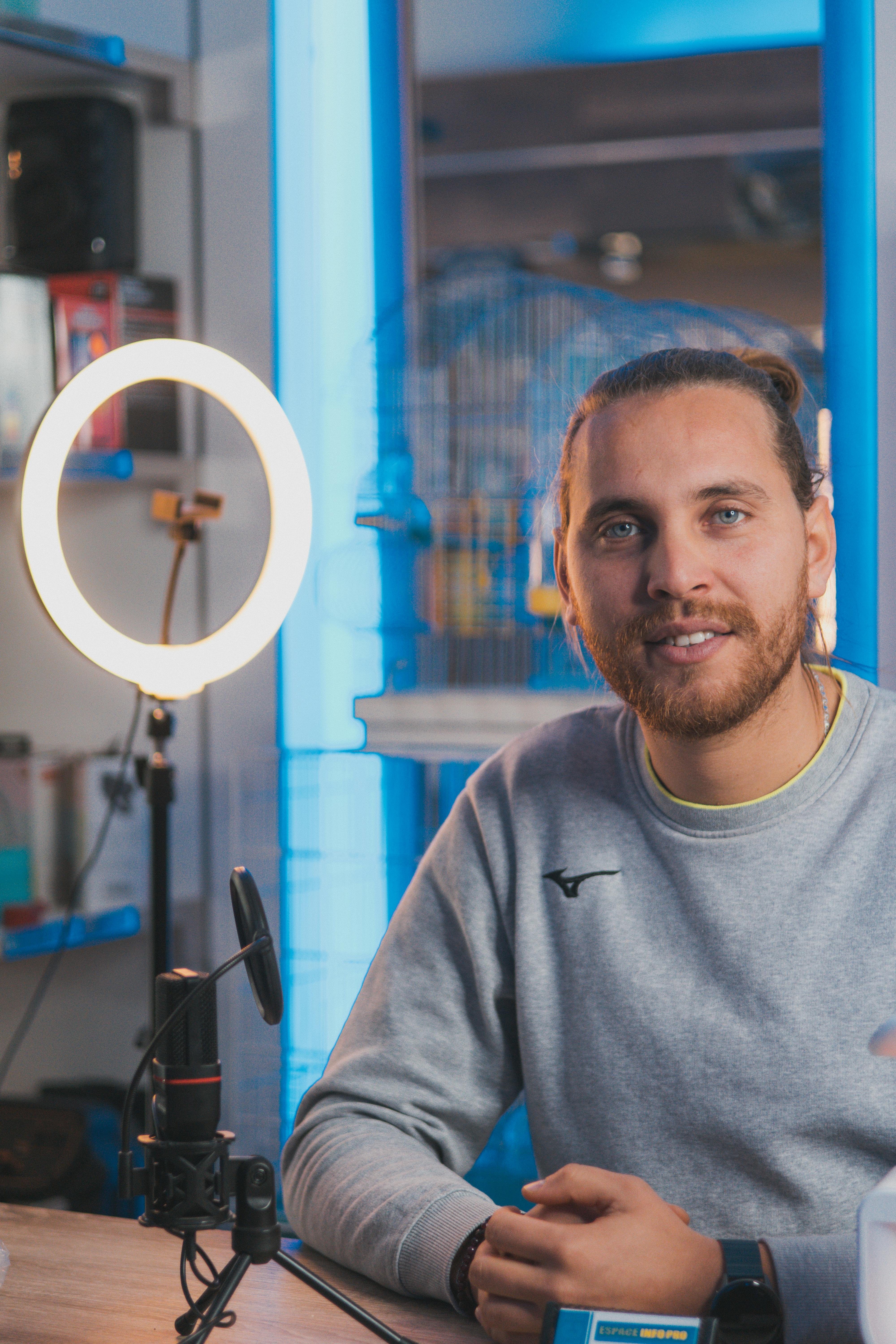 Young man podcasting with ring light and microphone in a modern studio setting. Captures creativity and technology.