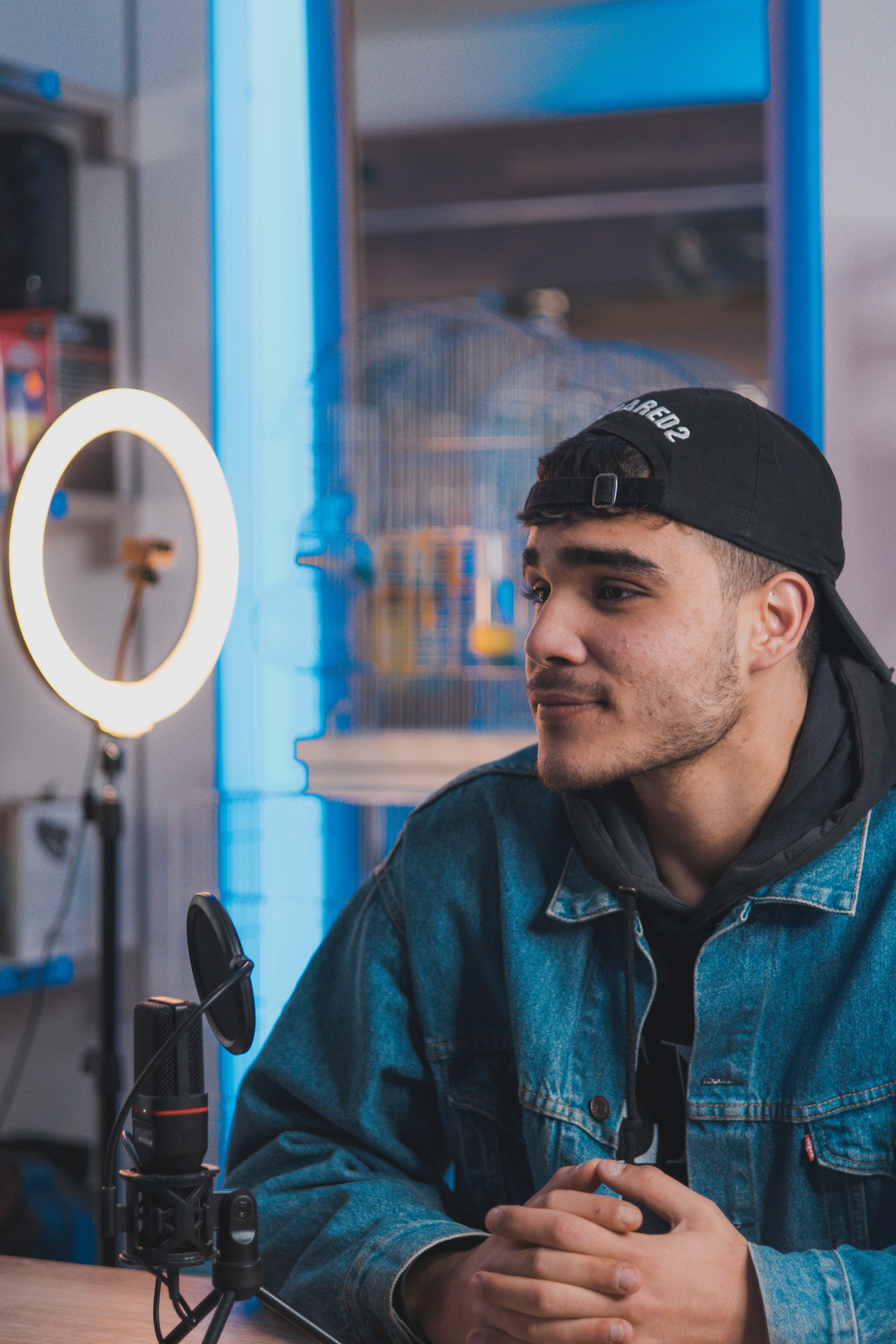 Stylish man in jean jacket poses indoors with photography lighting.