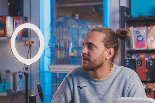 Man with long hair sitting in a tech store, illuminated by a ring light.