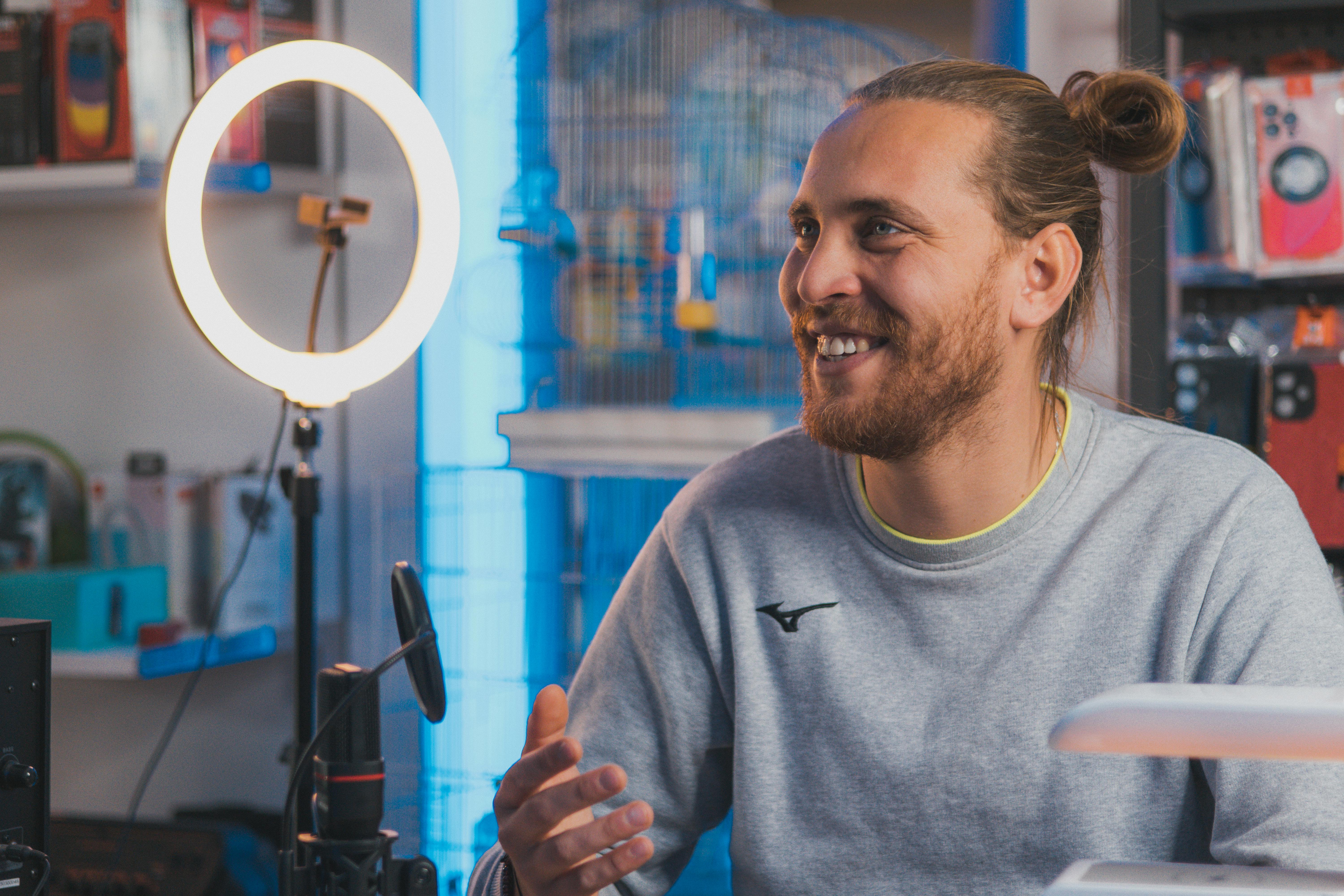 Smiling man with long hair recording content in a studio setting.