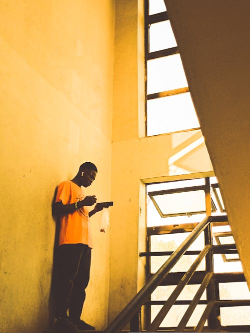 A Man Standing on a Staircase and Listening to Music on Earphones 