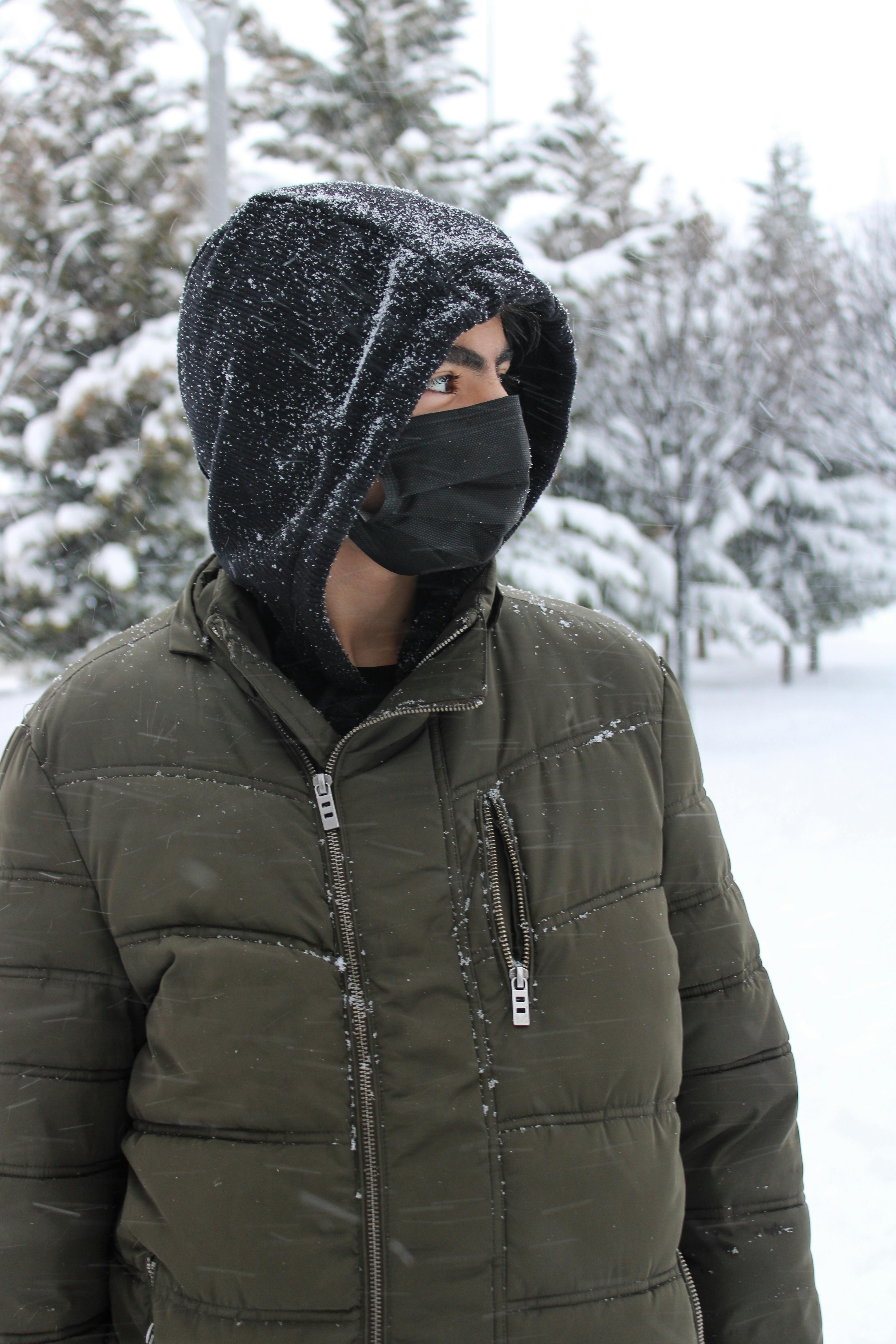 Man in a Hoodie and Jacket Wearing a Face Mask while Standing on a Snowy Field Free Stock Photo