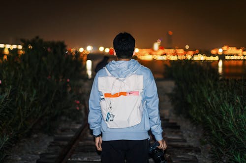 Back View of a Man Holding a Camera Walking at Night with City Lights in the Horizon 