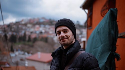 Free Portrait of a smiling man in a black jacket and beanie, standing outdoors in a cold setting. Stock Photo