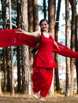A woman gracefully dances in a red dress in a sunlit forest, exuding joy and elegance.