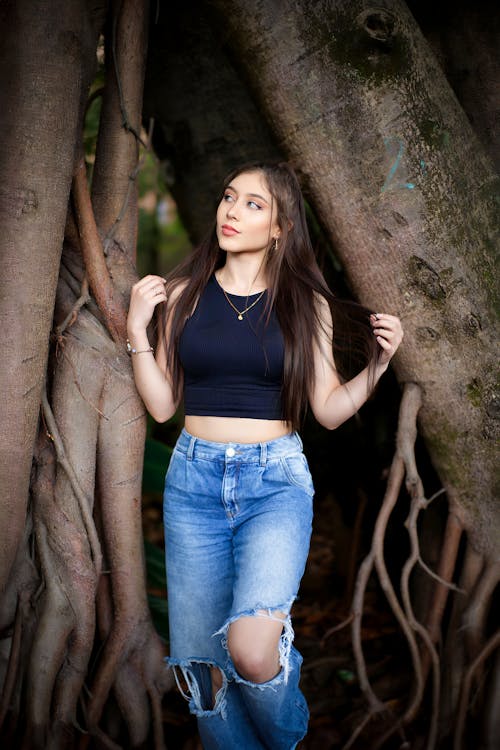 Woman in Torn Jeans Standing between Tree Roots