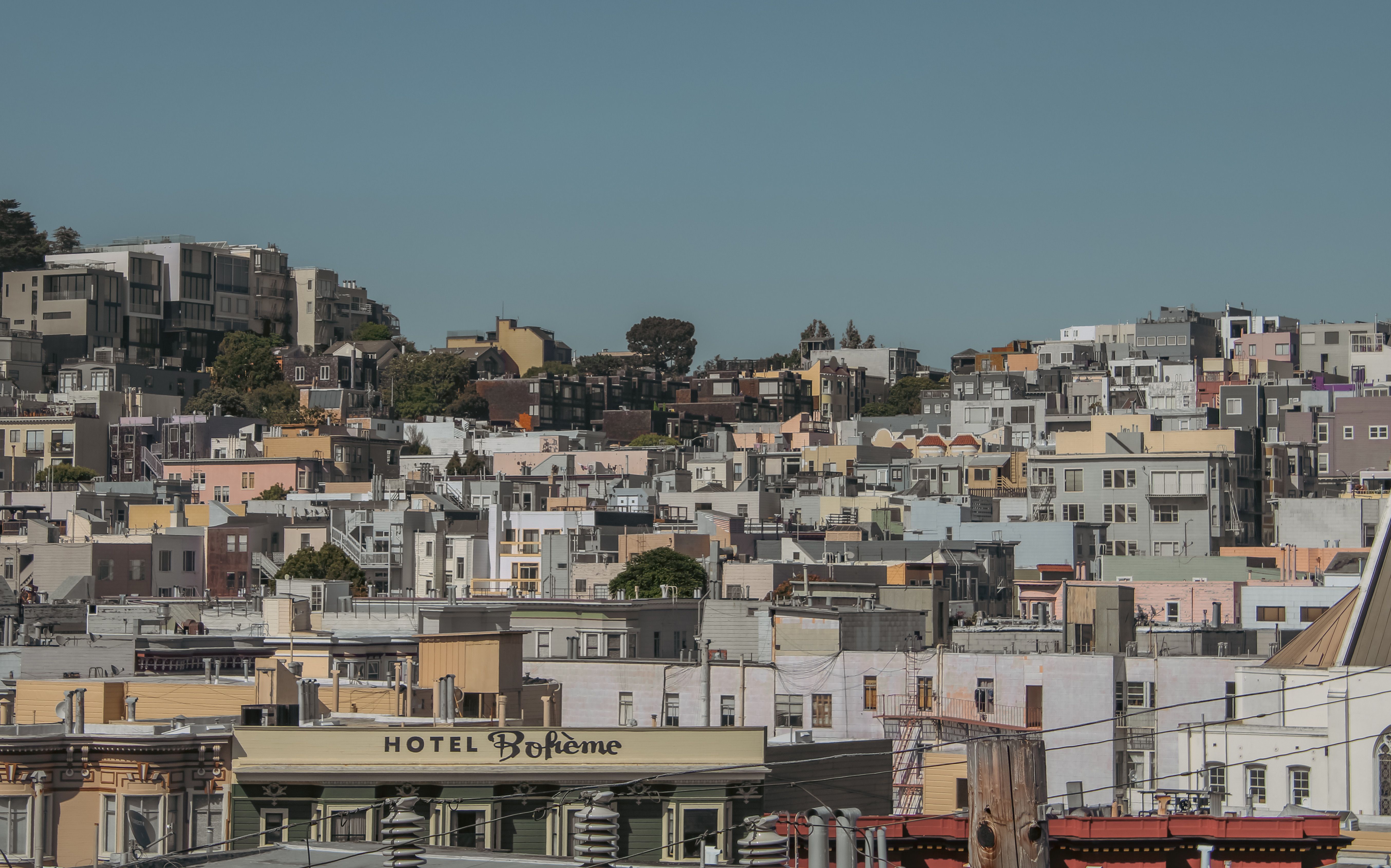Imagem de uma vista urbana com uma densa colagem de edifícios residenciais em uma colina, capturada sob um céu claro, ilustrando o cenário de uma cidade vibrante e movimentada.