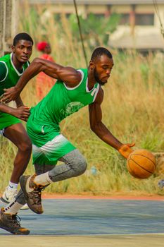 Two male athletes in green jerseys playing basketball outdoors.