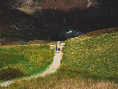 Free Group of hikers walking on a scenic mountain pathway, framed by lush greenery and dramatic hills. Stock Photo