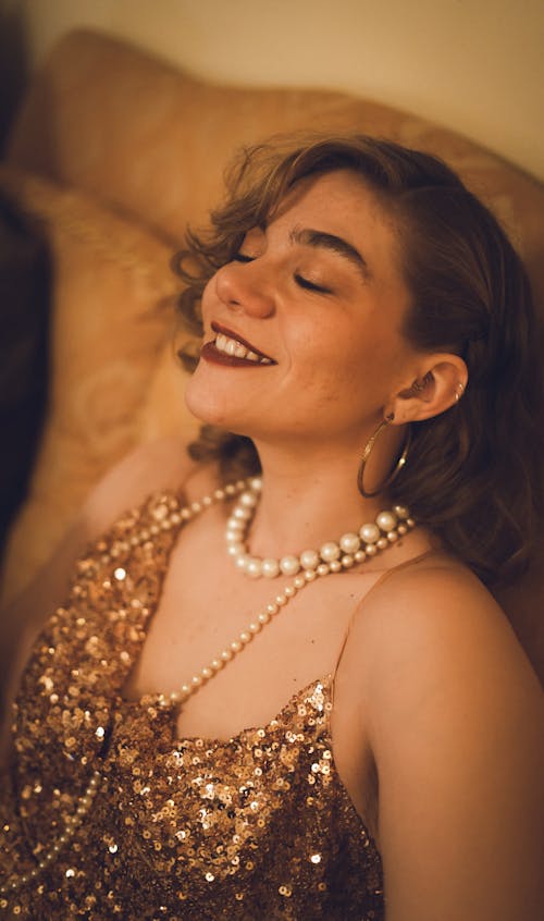 A woman in a gold dress smiling and laying on a couch