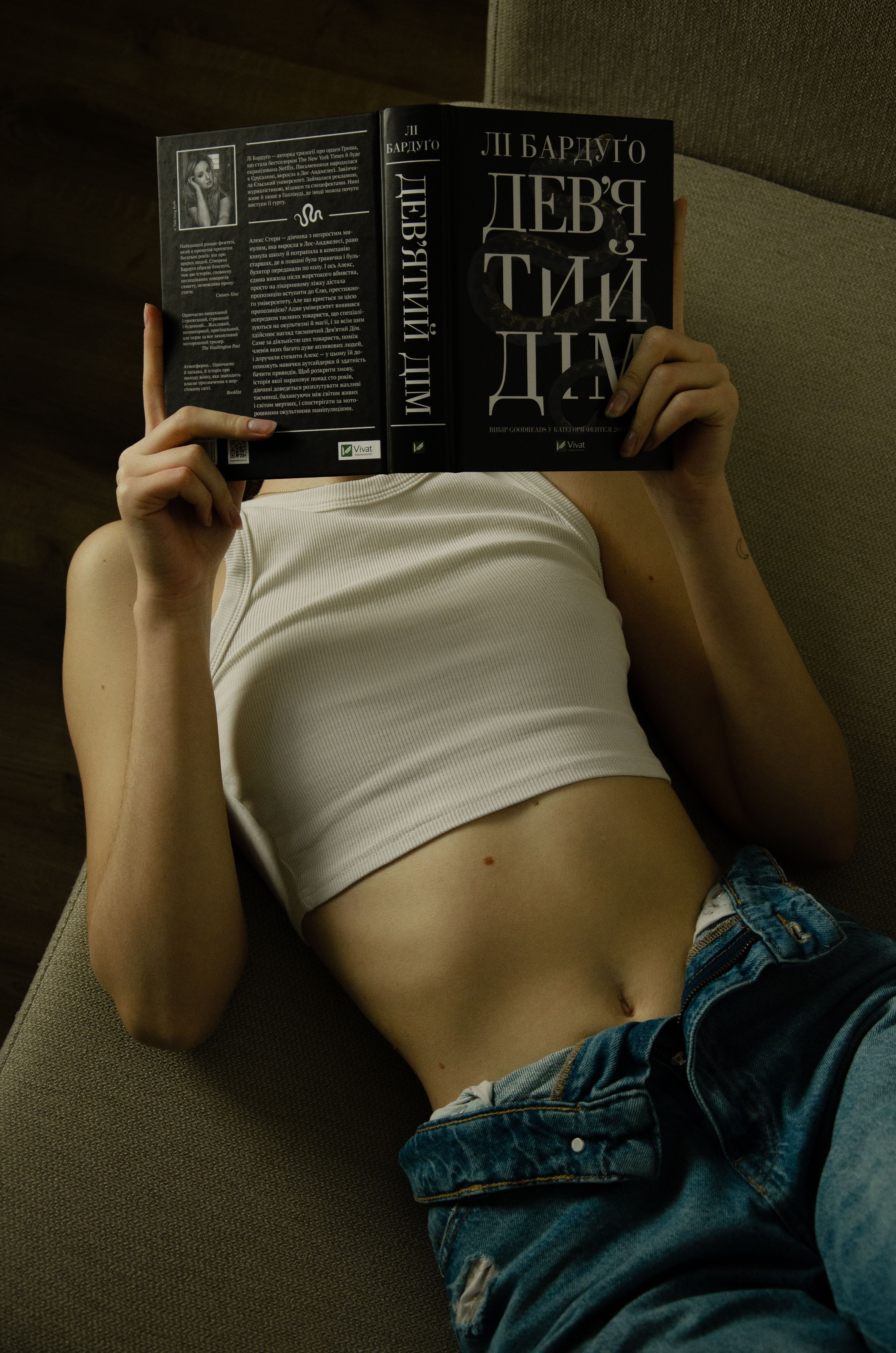A person in a casual outfit reading a book while lying on a sofa indoors.