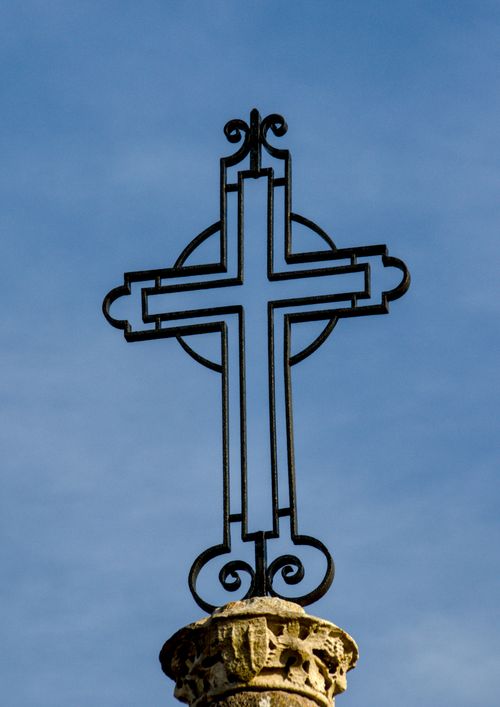 Free Silhouetted iron cross with ornate design against a clear blue sky, emphasizing religious symbolism. Stock Photo