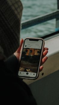 A person uses a smartphone to browse social media near a window.