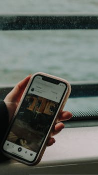 A person holding a smartphone by the window showing a social media app on a rainy day.