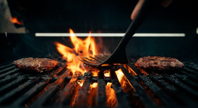 Sizzling beef patties on a flaming grill, perfect for summer BBQs.