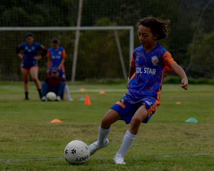 Young boy kicking soccer ball during practice on outdoor field with teammates.