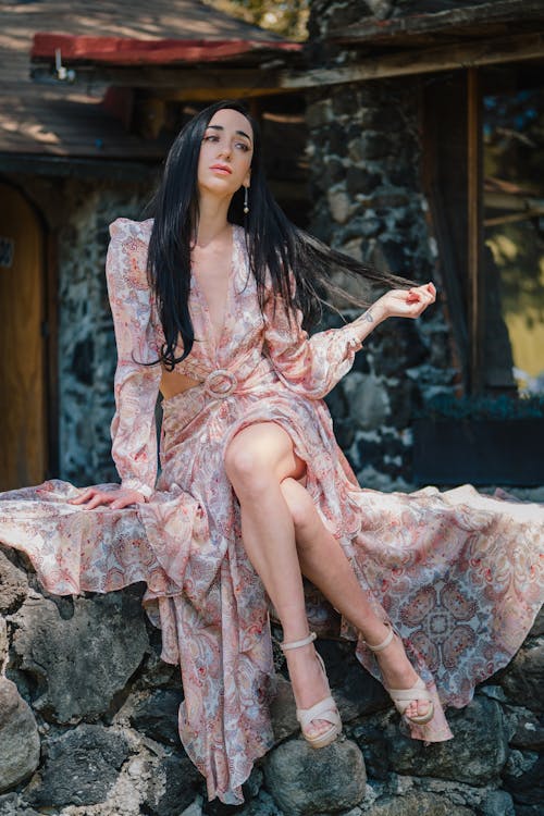 Woman in Floral Maxi Dress Sits on Stone Wall