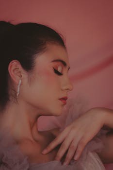 Side profile of a woman with closed eyes and artistic makeup against a pink background, exuding elegance and tranquility.