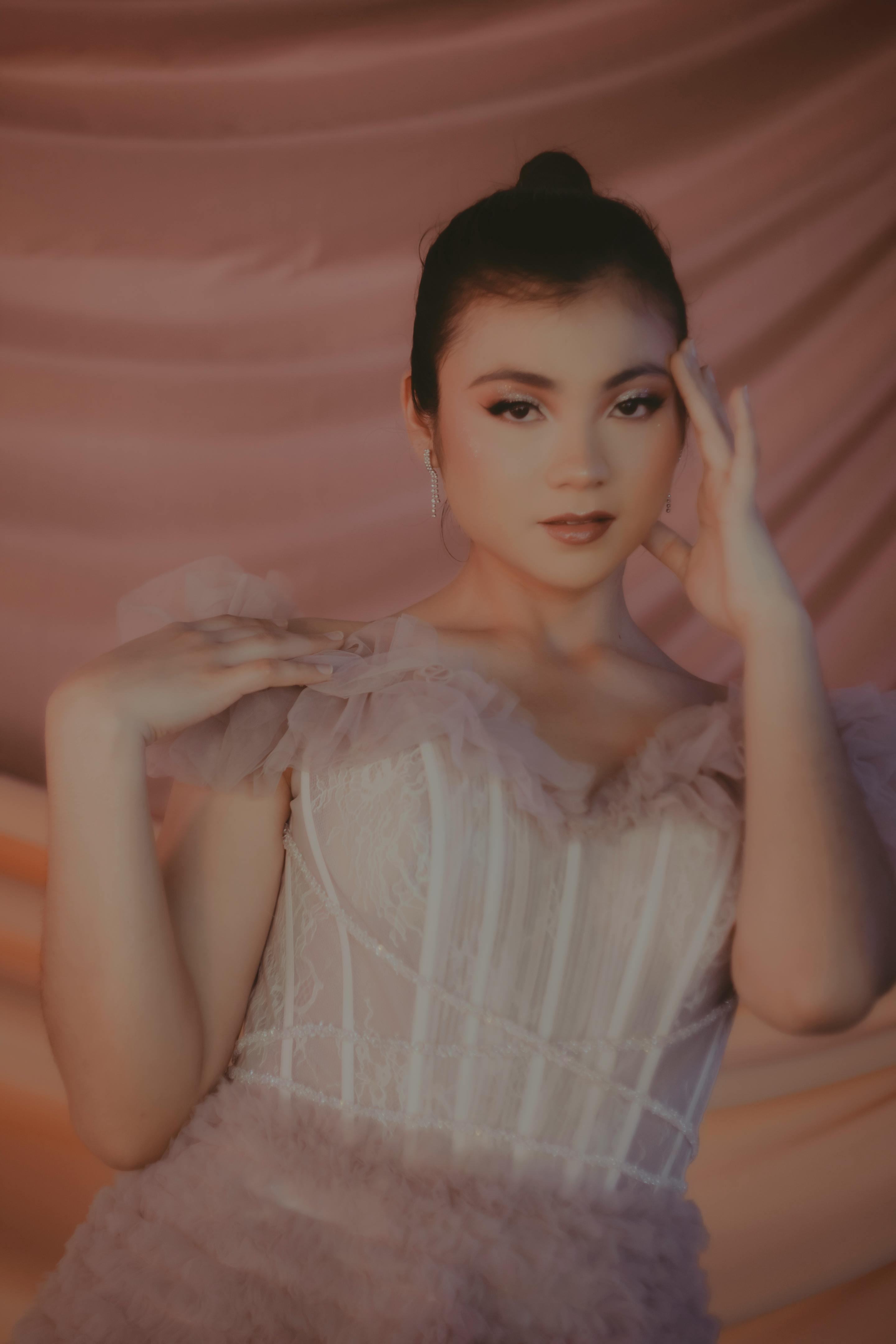 Chic young woman posing gracefully in a stylish pink dress with elegant ruffles, set against a soft draped background.
