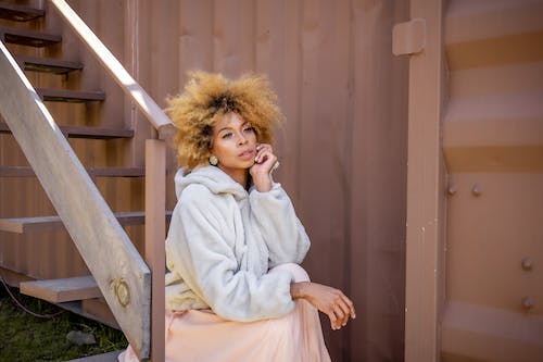 Woman in a Dress and Fuzzy Jacket Sitting on Steps Outside 