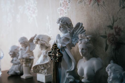 Elegant angel and bust figurines displayed on a decorative wall shelf with floral wallpaper.