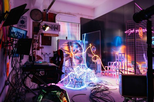 Colorful studio filled with neon lights, cables, and electronic equipment creating a futuristic ambiance.