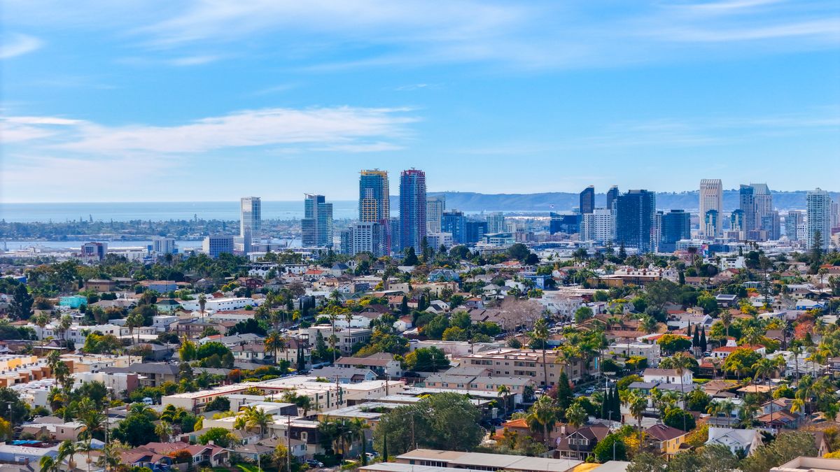 Aerial view of San Diego neighborhoods with the downtown skyline and bay behind them, for readers weighing Los Angeles vs. San Diego