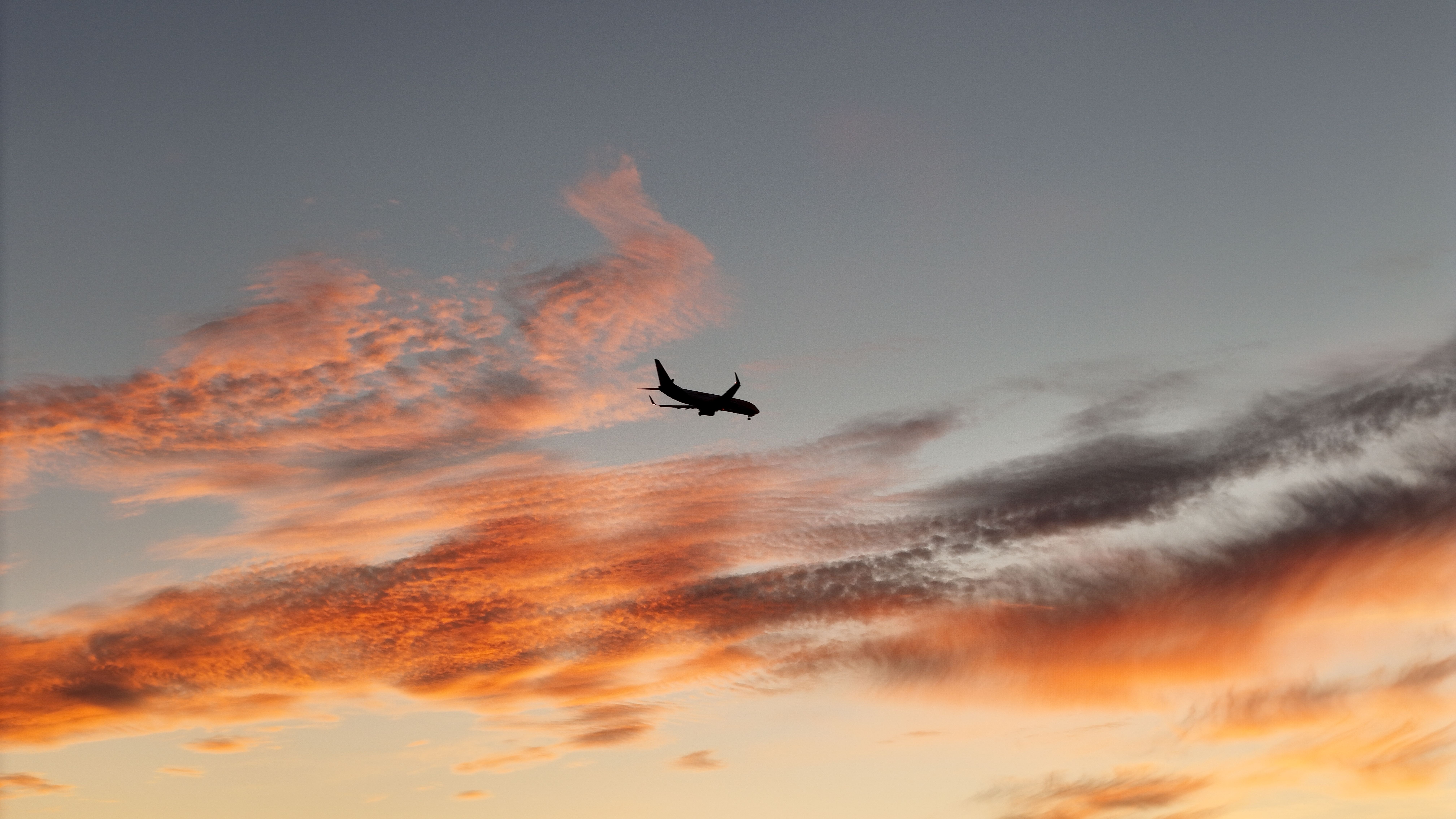 A striking image of a plane silhouette flying through a colorful sunset sky with vivid clouds.