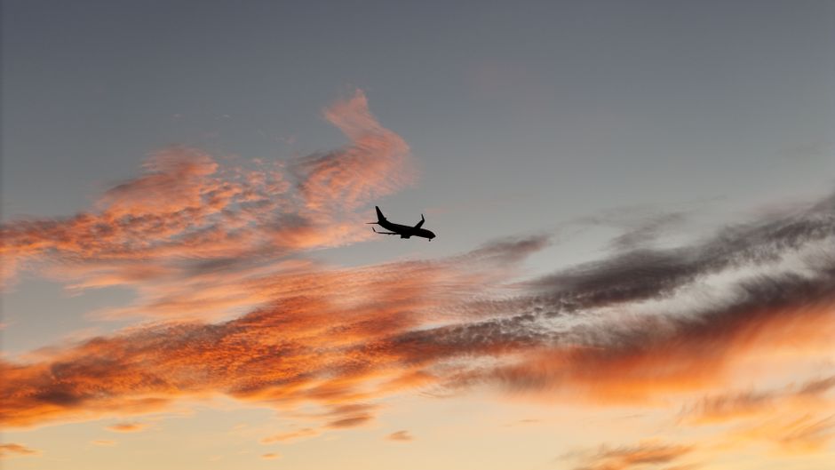 A striking image of a plane silhouette flying through a colorful sunset sky with vivid clouds.
