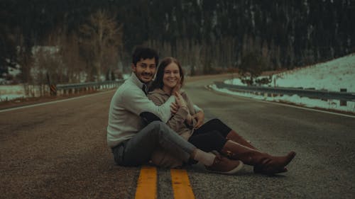 Smiling Couple Sitting and Hugging on Road in Winter