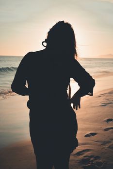 A serene silhouette of a woman standing on a sandy beach during a beautiful sunset.