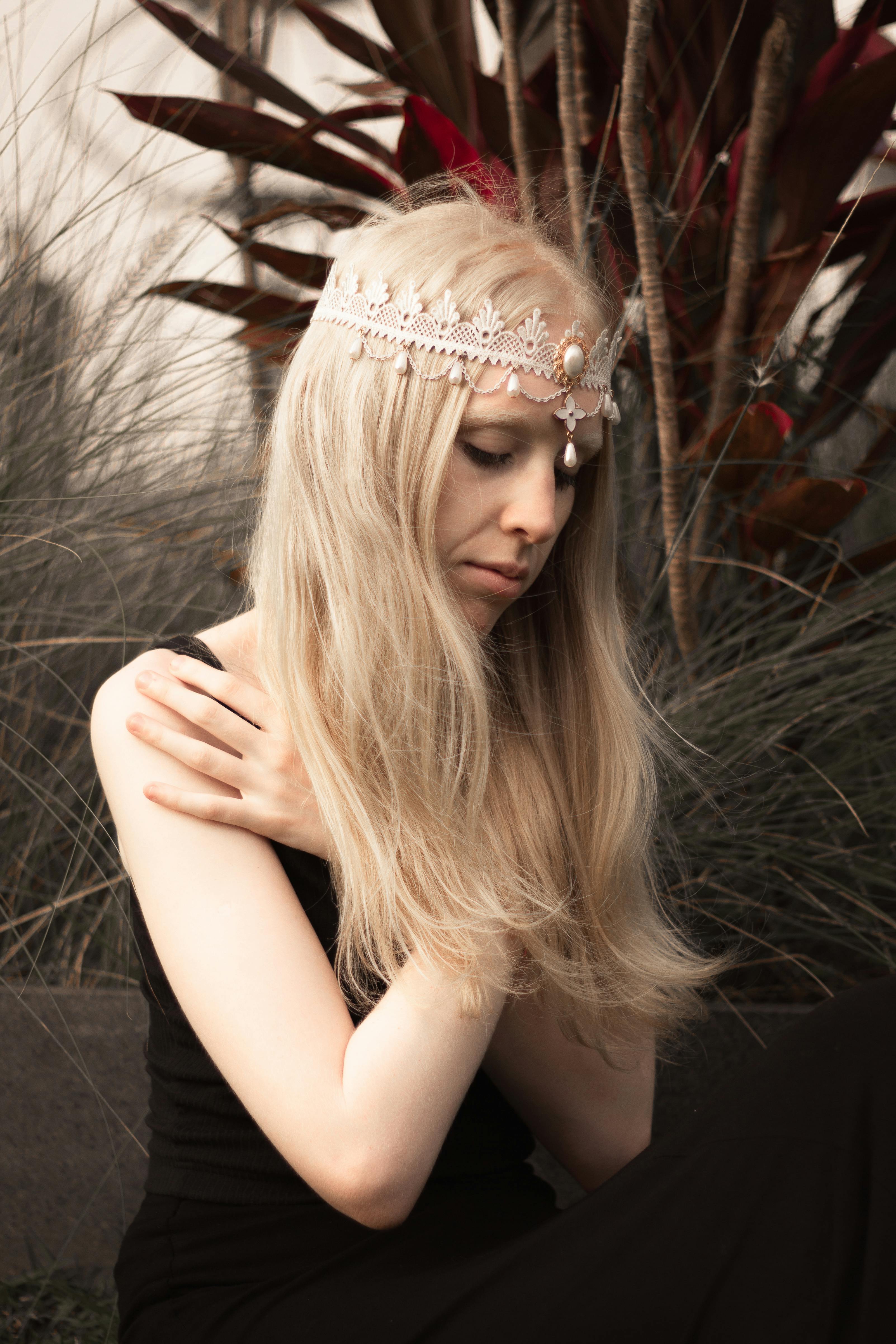 一位美丽的女子头戴饰物，在户外的高大植物间优雅地摆着姿势