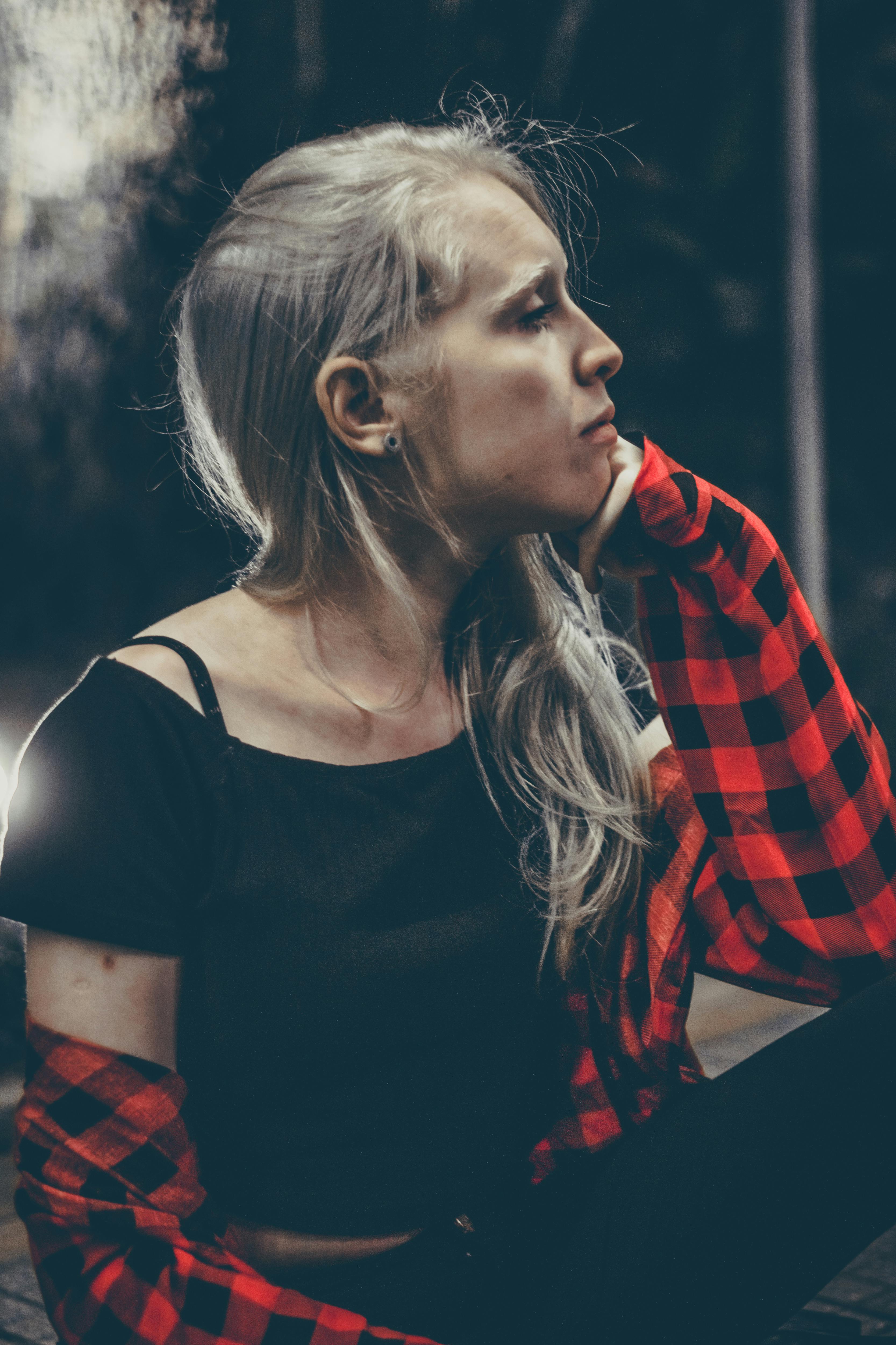 一名女子身穿红色格子衬衫，坐在户外，看起来若有所思