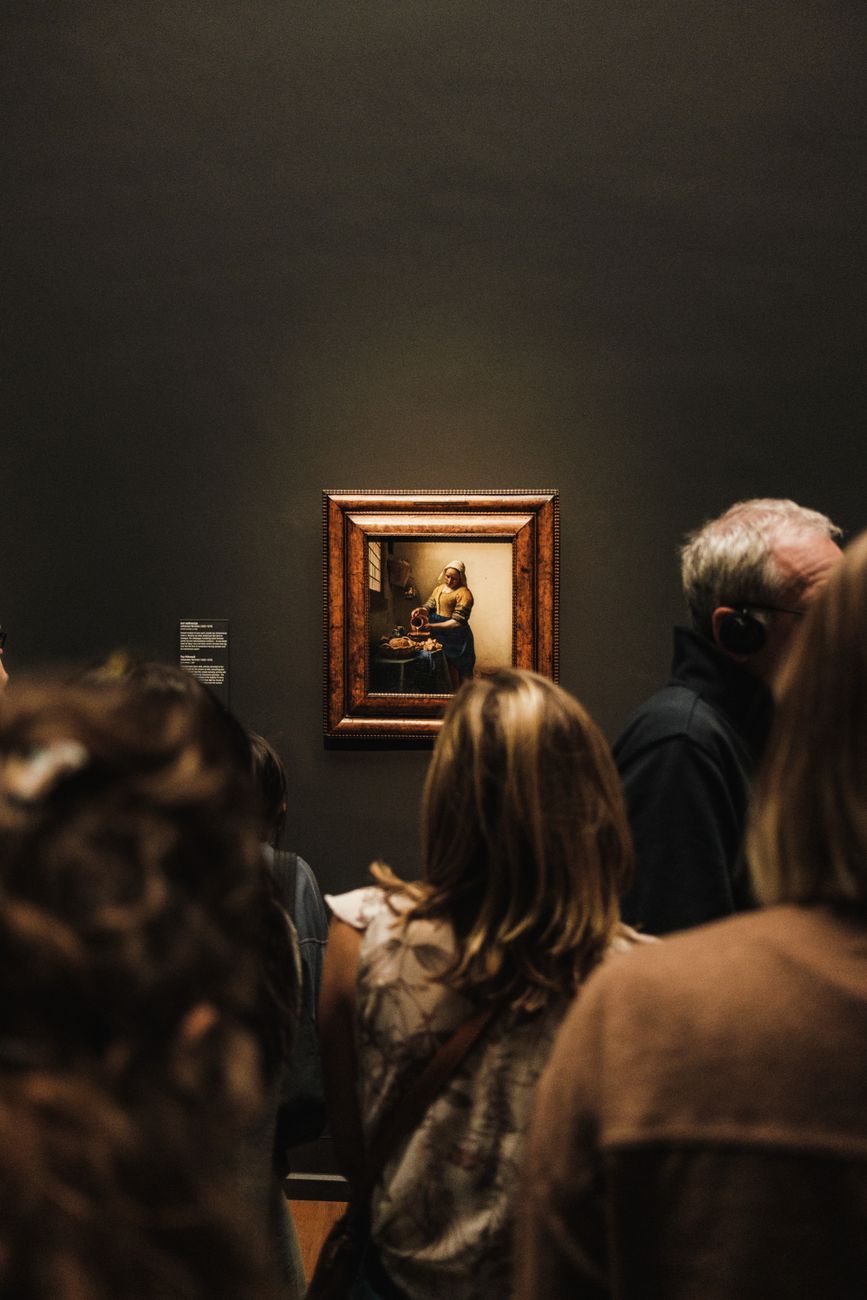 Menigte bekijkt een klassiek schilderij in een museum, wat een artistieke sfeer oproept.