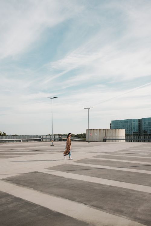 Free A woman strolls across a spacious, empty rooftop parking lot with city views. Stock Photo