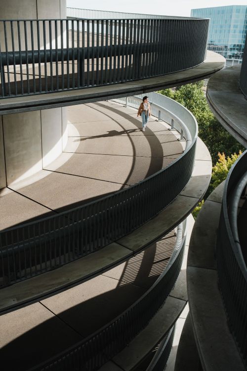 Free Woman walking along sunlit spiral walkway in urban setting, aerial perspective. Stock Photo