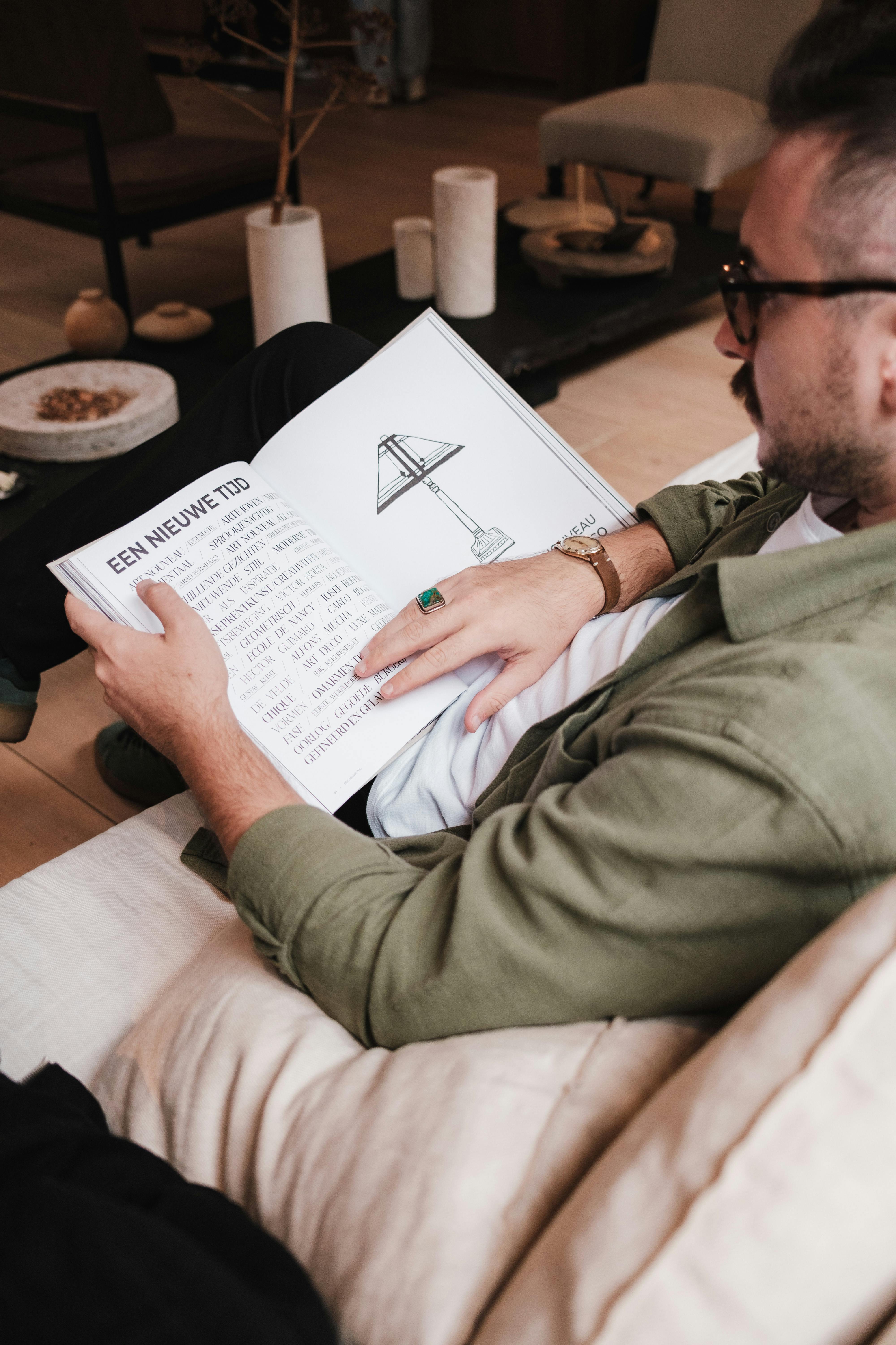 A man reading an illustrated book while comfortably seated on a sofa in a cozy living room.