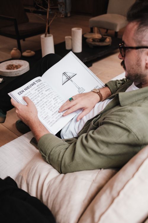Free A man reading an illustrated book while comfortably seated on a sofa in a cozy living room. Stock Photo
