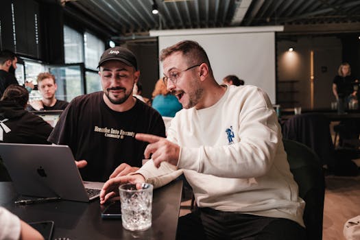 Two colleagues engaged in enthusiastic discussion over a laptop at a modern office.