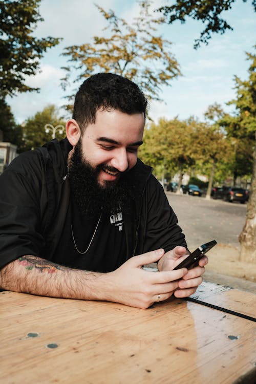 Smiling Man Sitting with Smartphone by Table
